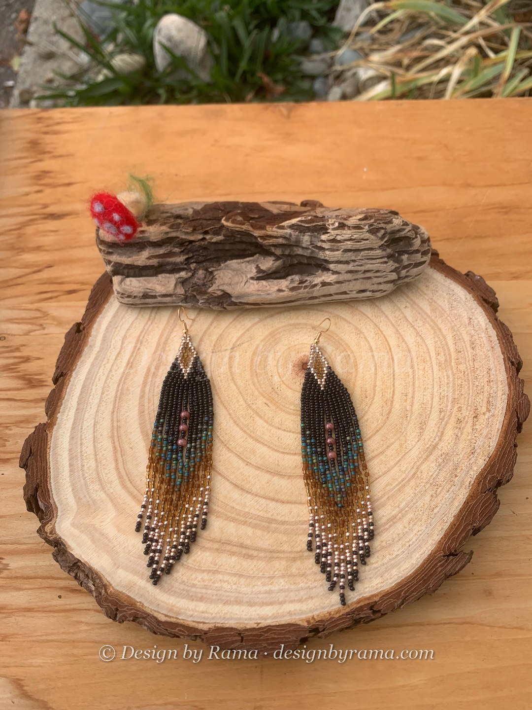Long triangular fringe drop earrings with jet black triangle apex, fringe transitioning through dusty teal, warm caramel, champagne gold, and black seed bead tips with mauve round accent beads mid-fringe, gold fish-hook closures.